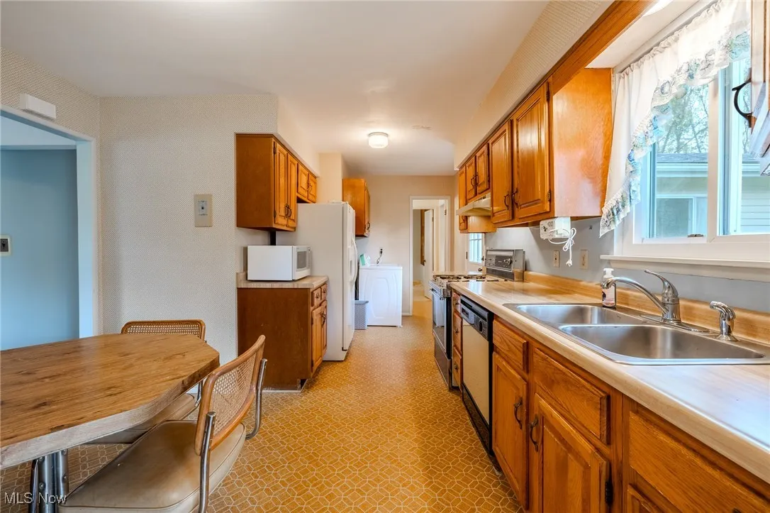 Kitchen with brown cabinets, light countertops, stove, white microwave, and stainless steel dishwasher