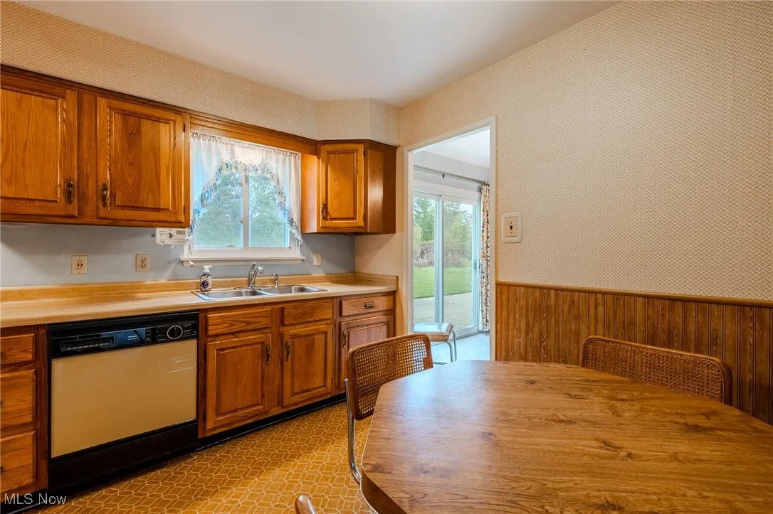 Kitchen with wainscoting, brown cabinetry, wooden walls, light countertops, and dishwashing machine