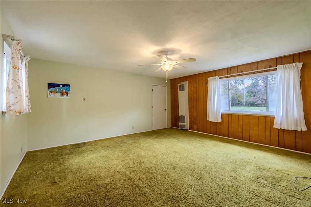 Spare room featuring carpet floors, wooden walls, a heating unit, and a ceiling fan