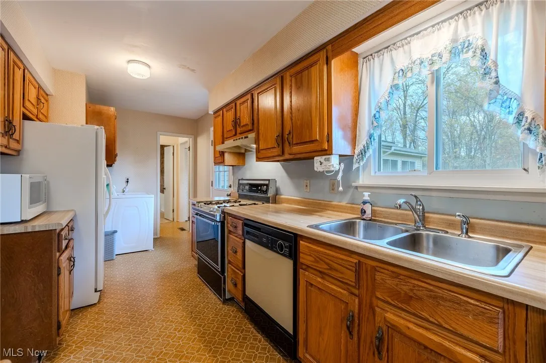 Kitchen with white appliances, brown cabinets, light countertops, and under cabinet range hood