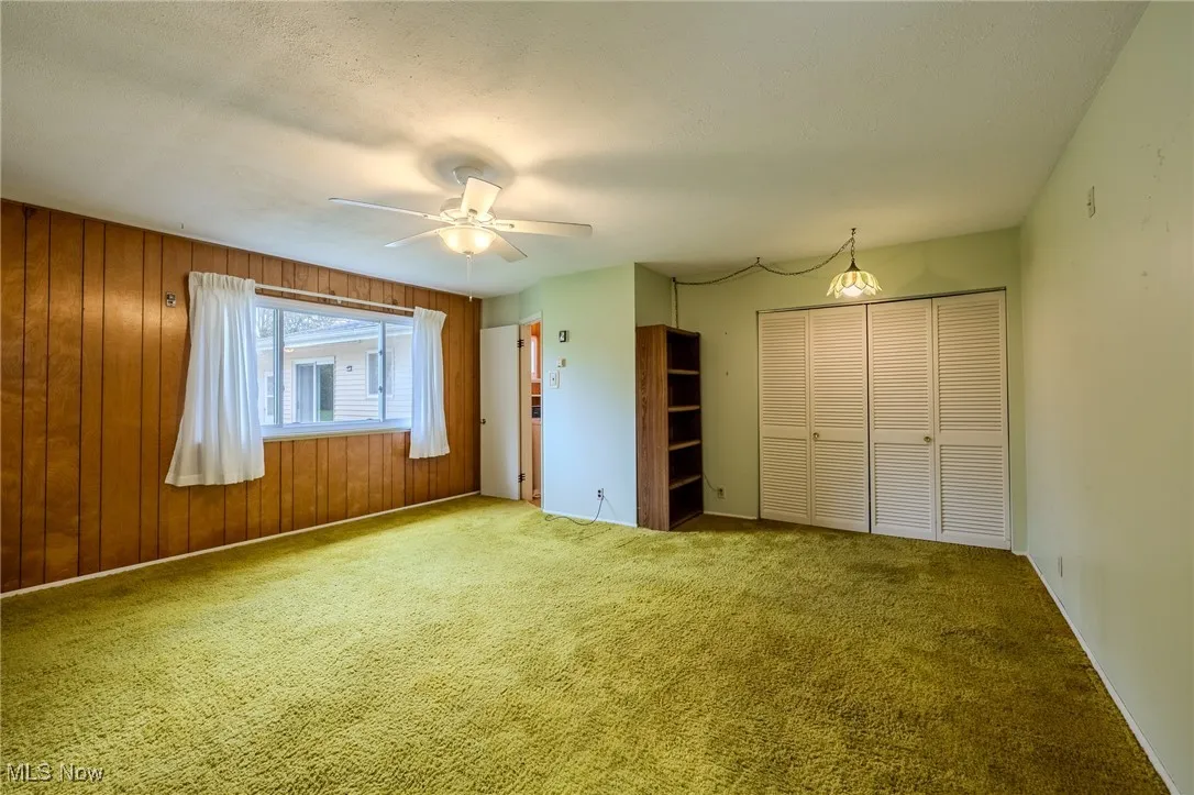 Unfurnished bedroom with a closet, carpet, a ceiling fan, and wood walls