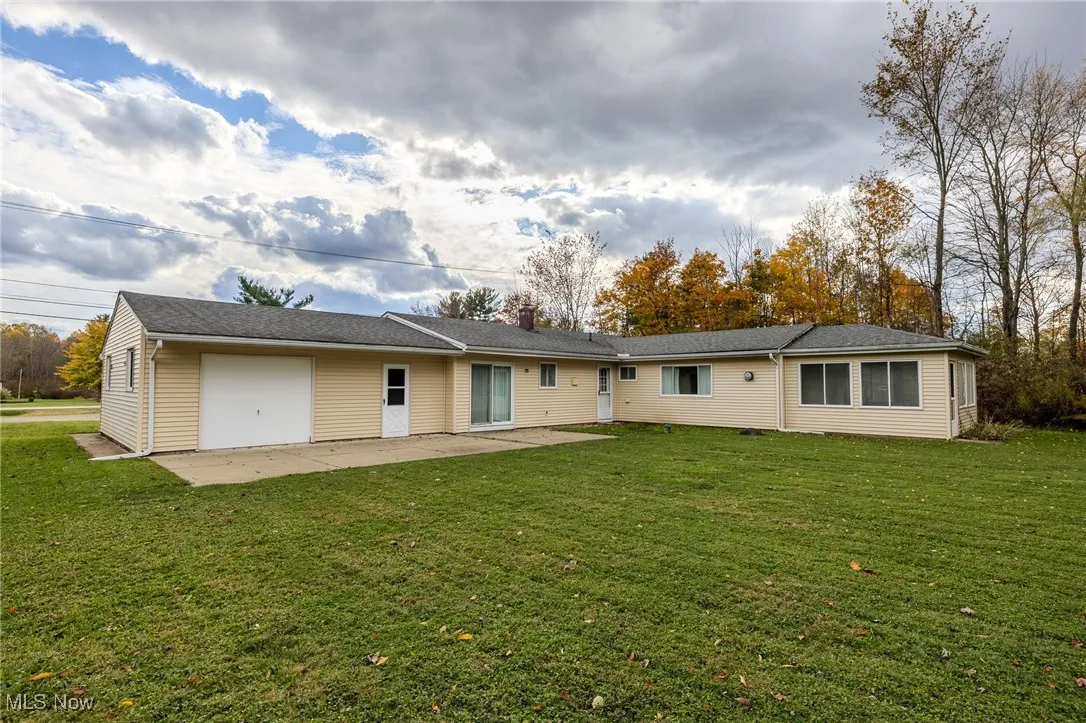 Back of property with a lawn, a patio, a garage, and roof with shingles