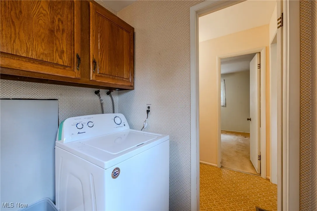 Washroom with washer / clothes dryer, wallpapered walls, and cabinet space