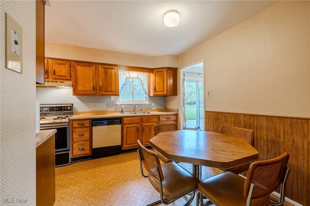 Kitchen featuring wood walls, a wainscoted wall, light countertops, brown cabinetry, and dishwashing machine