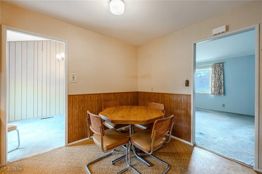 Dining area featuring wood walls, carpet floors, and a wainscoted wall