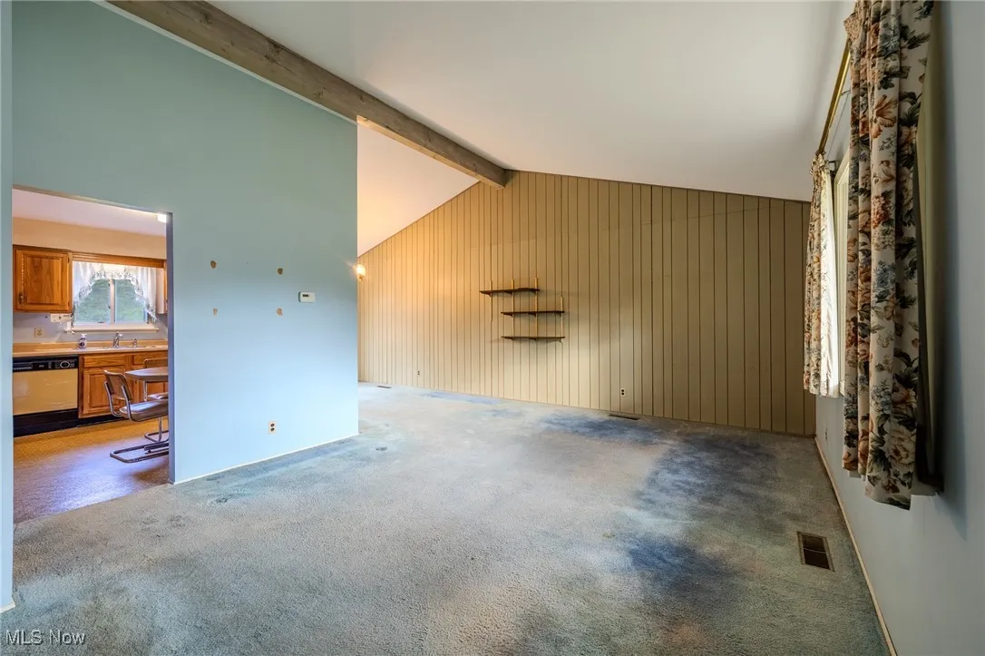 Unfurnished living room with beamed ceiling, carpet floors, wooden walls, and high vaulted ceiling