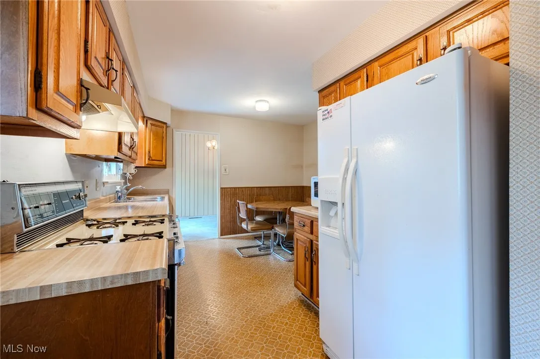Kitchen with a wainscoted wall, white appliances, light countertops, wood walls, and brown cabinetry