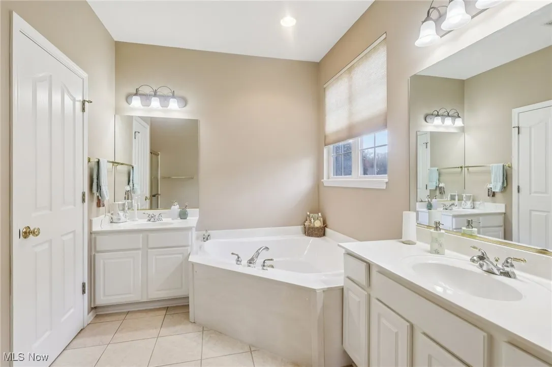 Full bath featuring two vanities, light tile patterned floors, and a bath