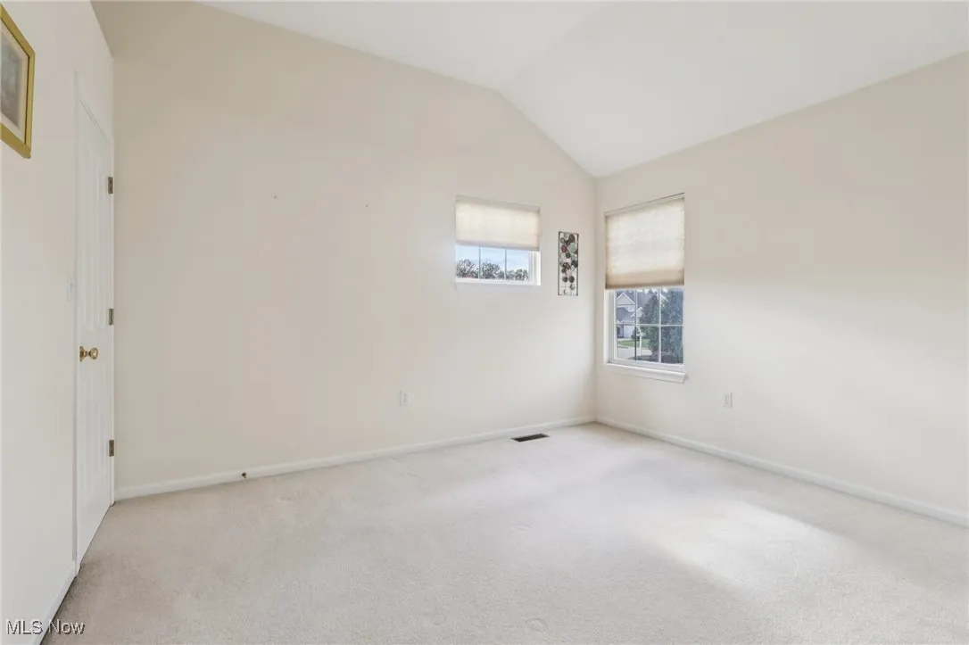 Carpeted spare room featuring lofted ceiling and baseboards
