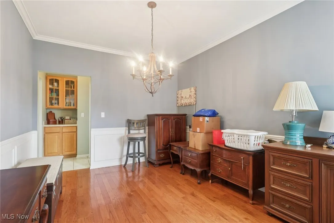 Sitting room with ornamental molding, a chandelier, light wood-type flooring, wainscoting, and a decorative wall