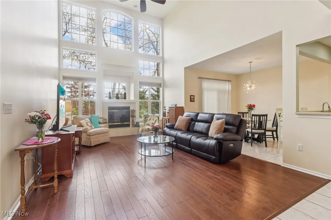 Living room with ceiling fan, wood finished floors, a high ceiling, a chandelier, and a tile fireplace