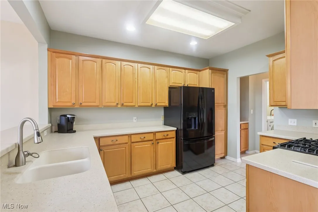 Kitchen with black refrigerator with ice dispenser, light tile patterned floors, light stone countertops, and light brown cabinets