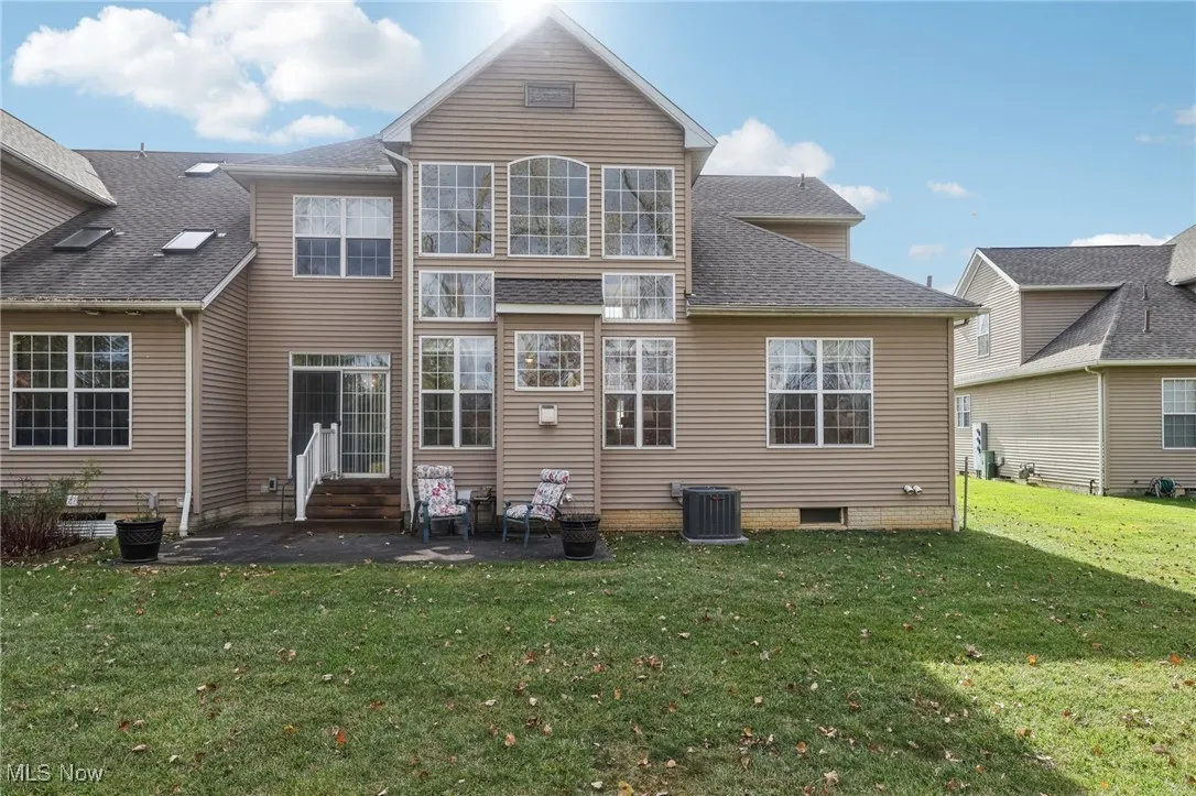 Rear view of property featuring a patio, roof with shingles, a lawn, and entry steps