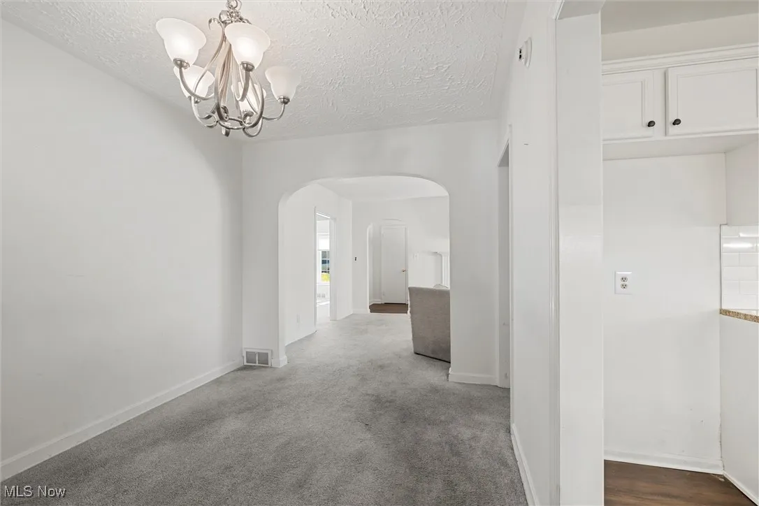 Dining area arched walkways, carpet, a textured ceiling, and a chandelier