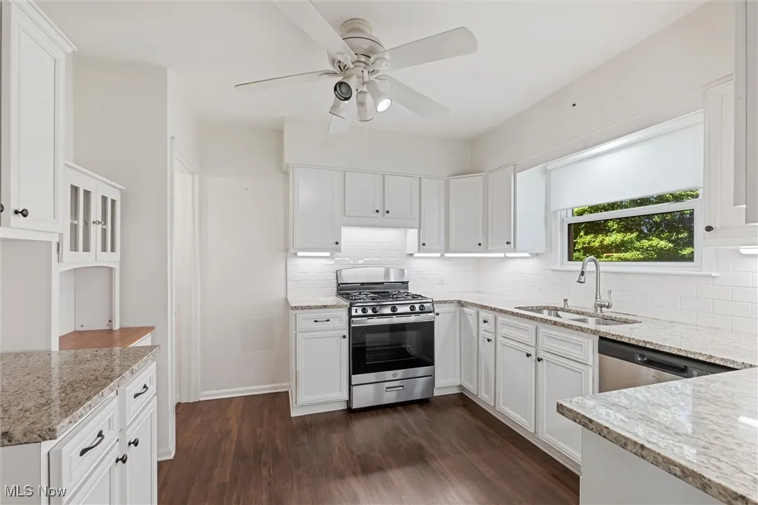 Kitchen featuring appliances with stainless steel finishes, white cabinets, light stone counters, dark wood-style floors, and backsplash