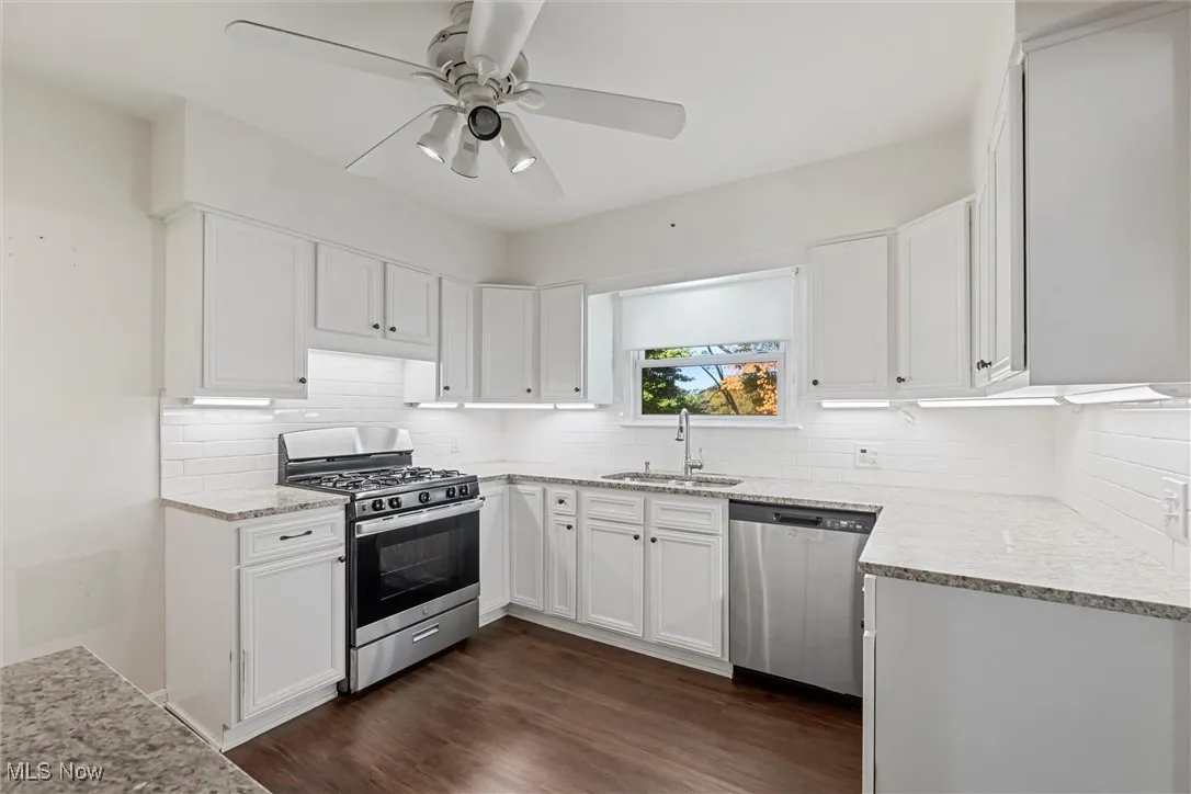 Kitchen with stainless steel appliances, white cabinetry, and light stone counters