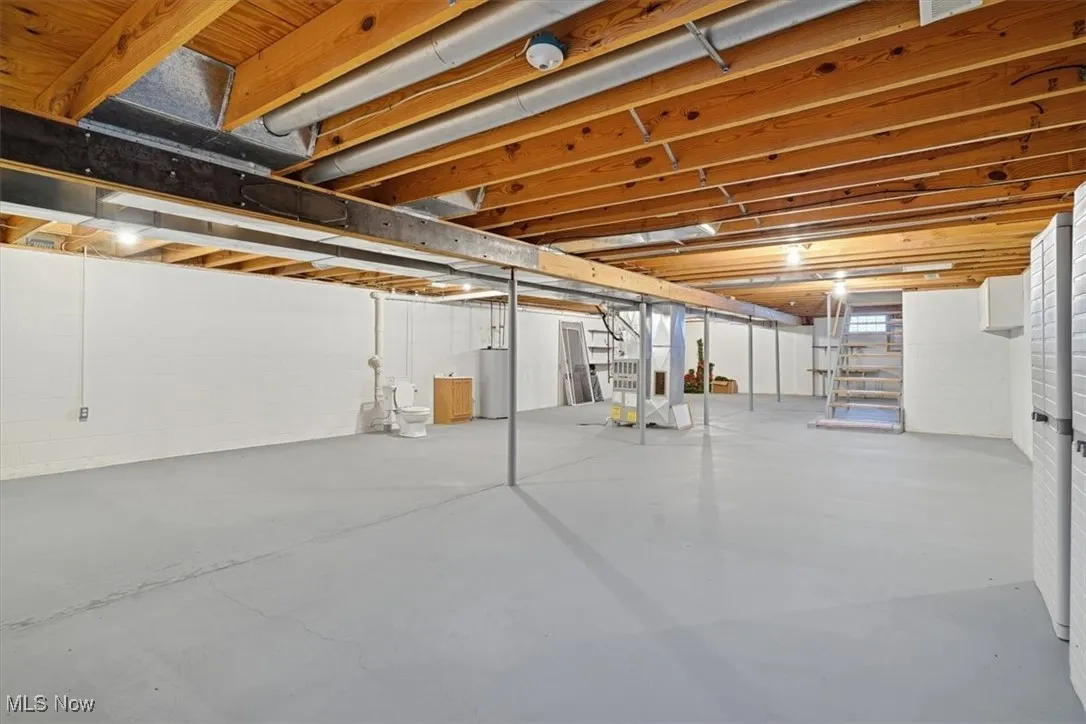 Unfinished basement featuring stairs and water heater