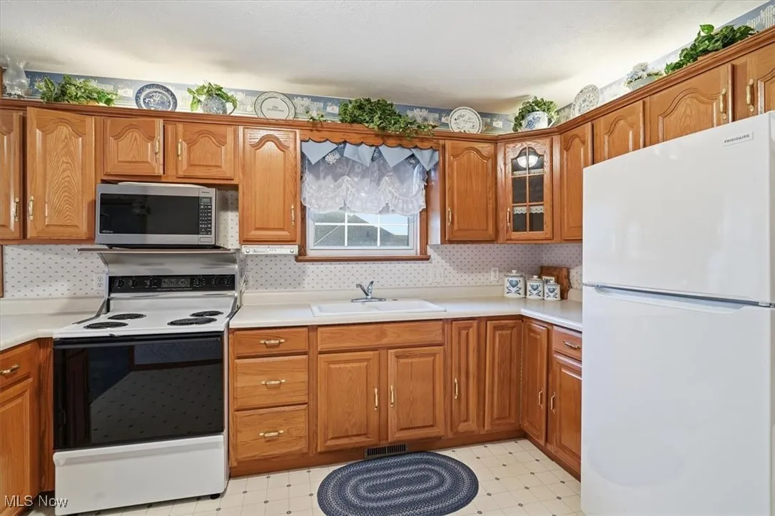 Kitchen featuring freestanding refrigerator, range with electric cooktop, brown cabinetry, stainless steel microwave, and light countertops