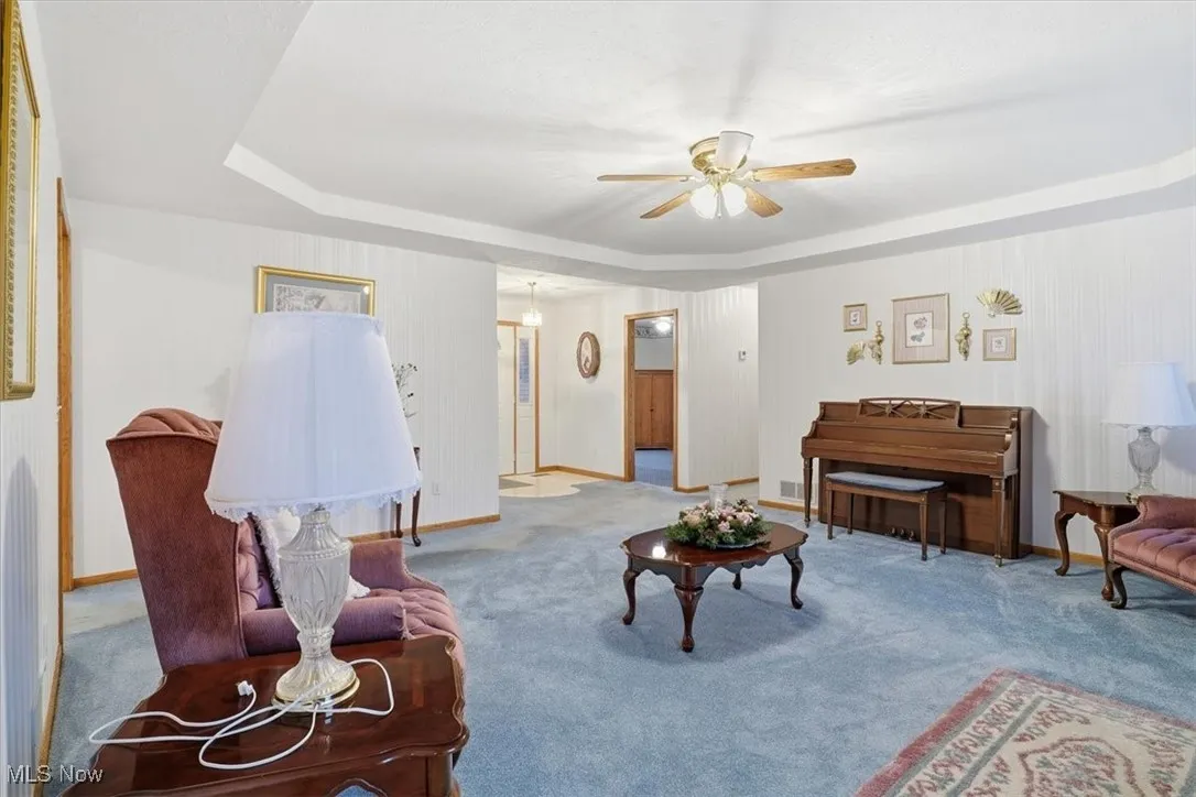 Living room featuring a raised ceiling, carpet flooring, and ceiling fan