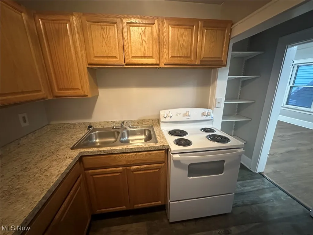 Kitchen featuring white range with electric stovetop, light countertops, brown cabinetry, and dark wood finished floors