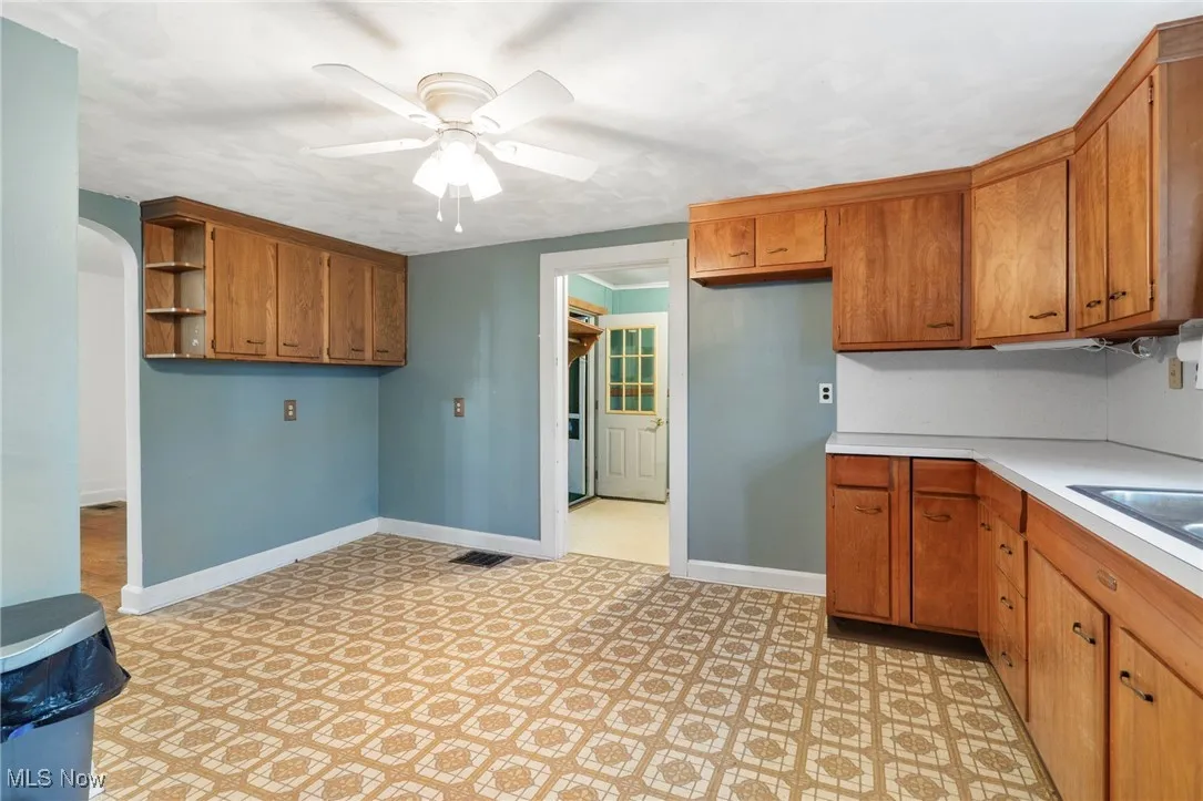 Kitchen with brown cabinets, arched walkways, light countertops, ceiling fan, and open shelves