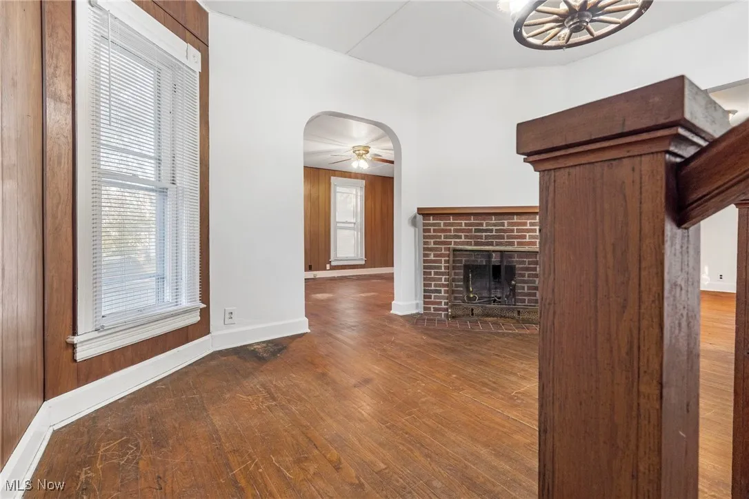 Unfurnished living room featuring arched walkways, dark wood-style floors, plenty of natural light, and a brick fireplace