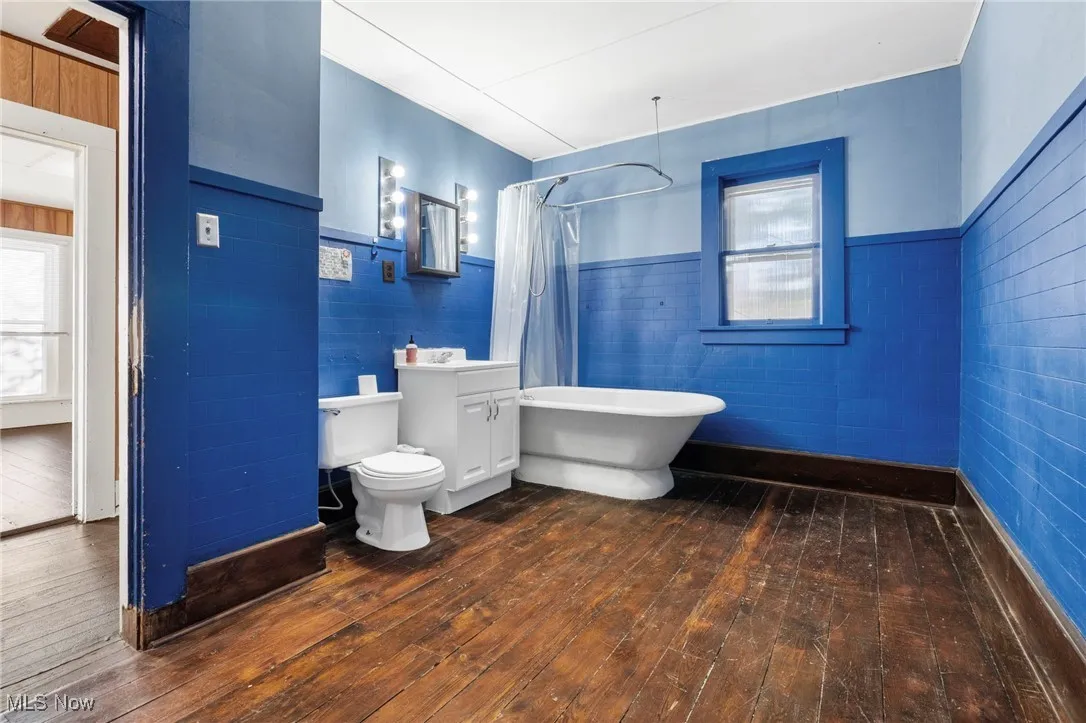 Bathroom featuring dark wood-style flooring, wainscoting, and tile walls