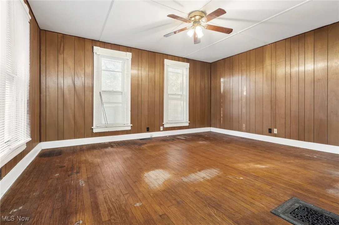 Empty room featuring hardwood / wood-style floors, wooden walls, and a ceiling fan