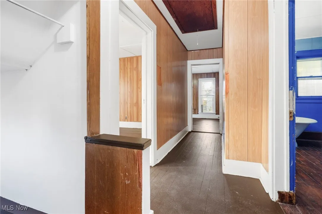 Hall with attic access, dark wood-type flooring, and wood walls