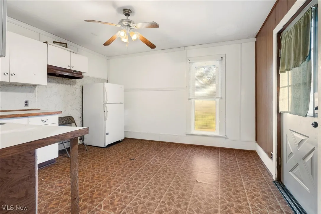 Kitchen featuring freestanding refrigerator, white cabinets, light countertops, dark floors, and ornamental molding