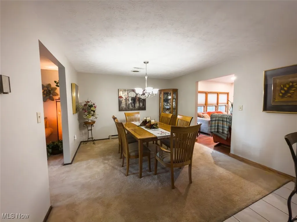 Dining space featuring a textured ceiling, a chandelier, light colored carpet, and light tile patterned floors