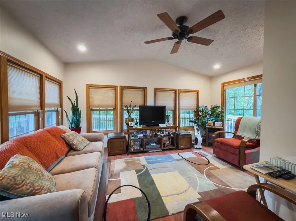 Living room featuring a textured ceiling, vaulted ceiling, a ceiling fan, wood finished floors, and recessed lighting