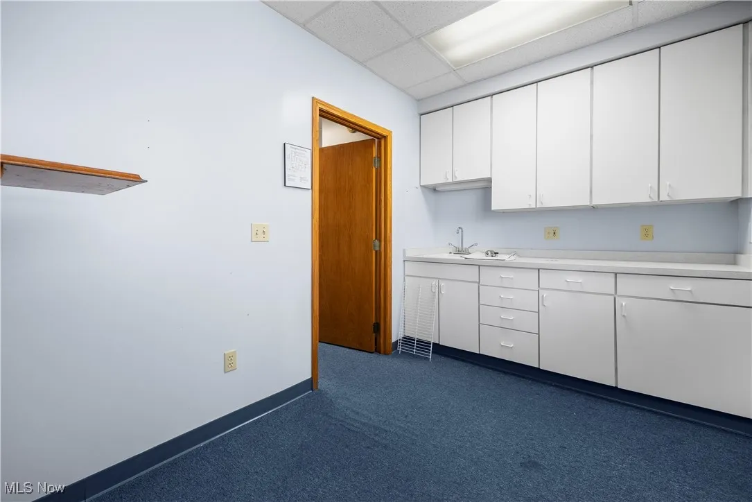 Kitchen featuring light countertops, a paneled ceiling, white cabinets, and dark colored carpet