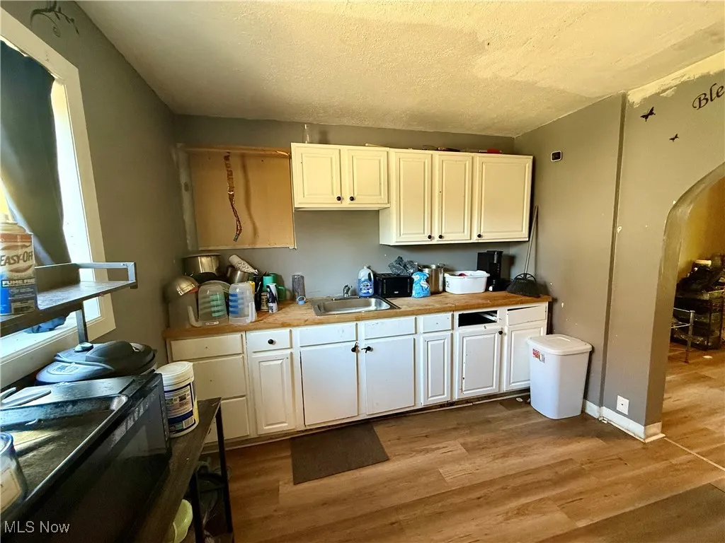 Kitchen with arched walkways, dark wood-type flooring, a textured ceiling, and white cabinets