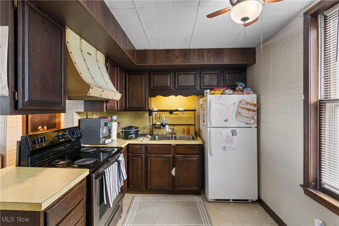 Kitchen with range with electric stovetop, dark brown cabinetry, freestanding refrigerator, light countertops, and under cabinet range hood