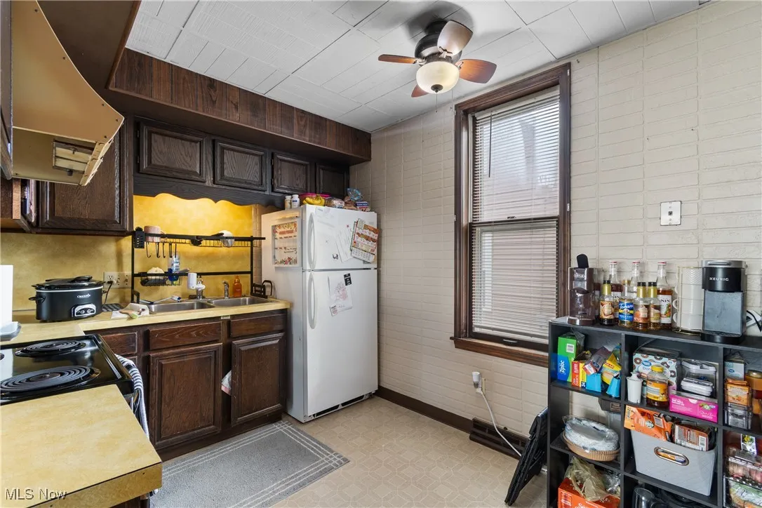 Kitchen featuring dark brown cabinets, light countertops, range hood, freestanding refrigerator, and a ceiling fan