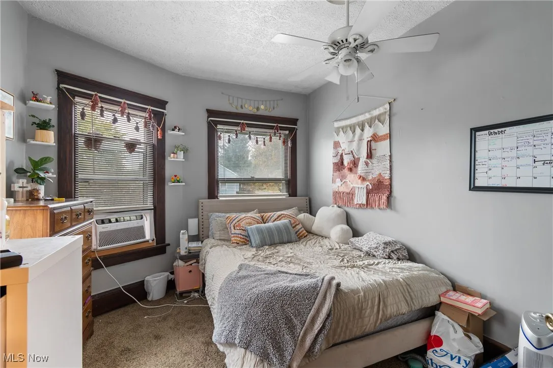 Carpeted bedroom with a textured ceiling, ceiling fan, and cooling unit