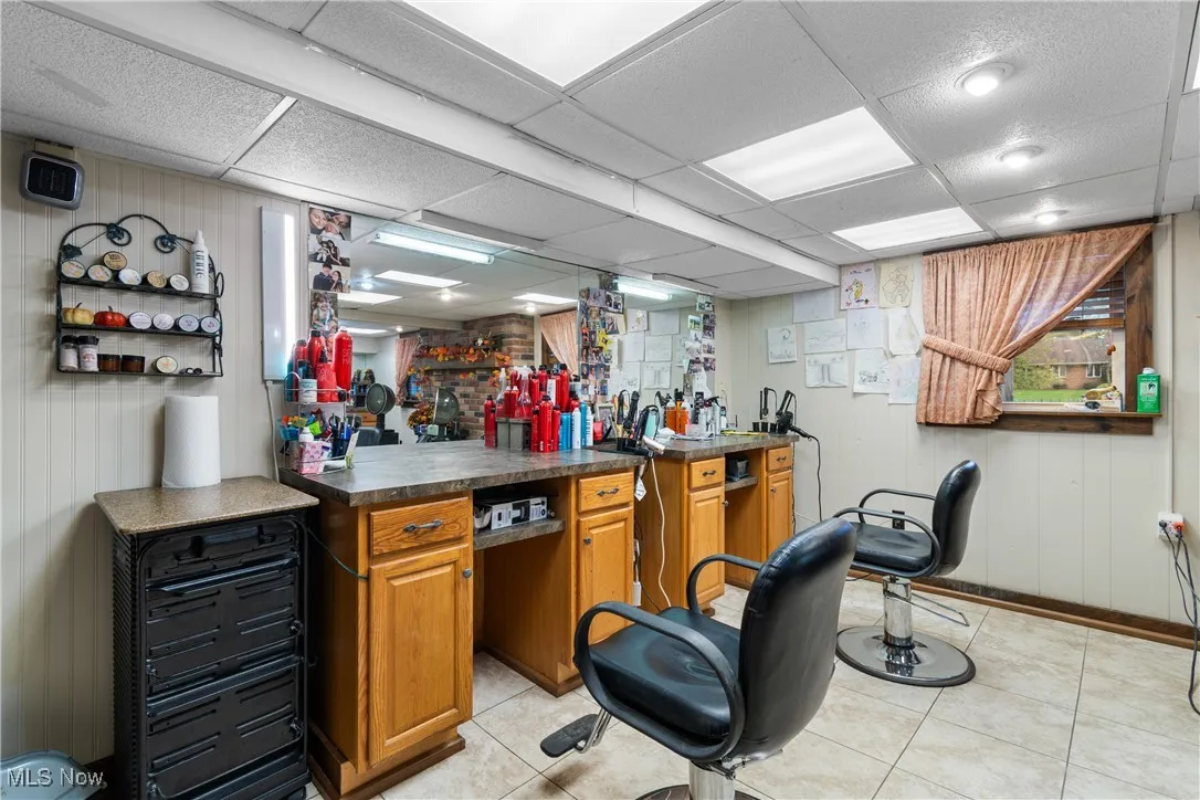 Bar featuring wooden walls, dark countertops, brown cabinets, light tile patterned flooring, and a drop ceiling