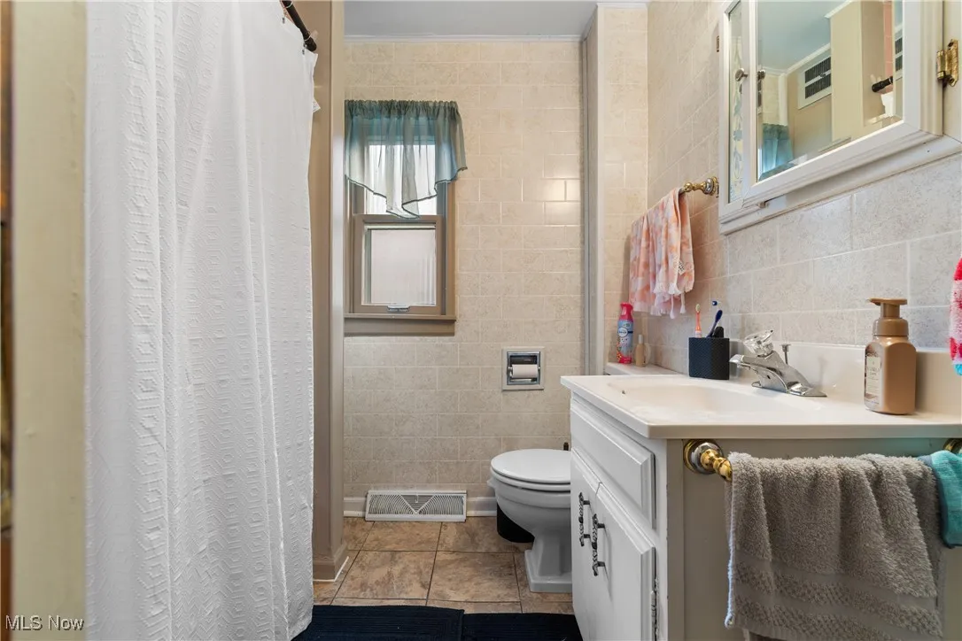 Full bathroom with tile walls, vanity, curtained shower, and tile patterned floors