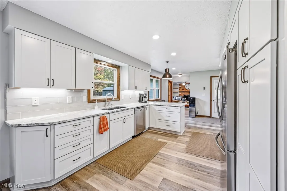 Kitchen featuring decorative backsplash, white cabinetry, a peninsula, light stone countertops, and recessed lighting
