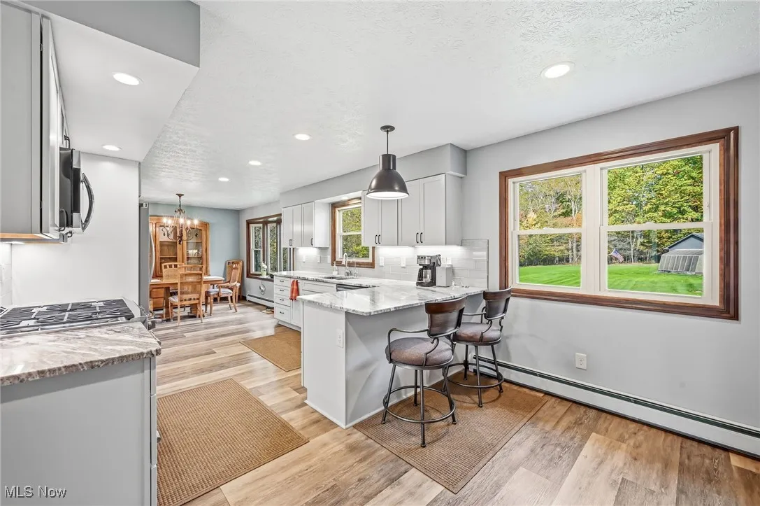 Kitchen featuring light stone countertops, pendant lighting, a peninsula, light wood finished floors, and recessed lighting