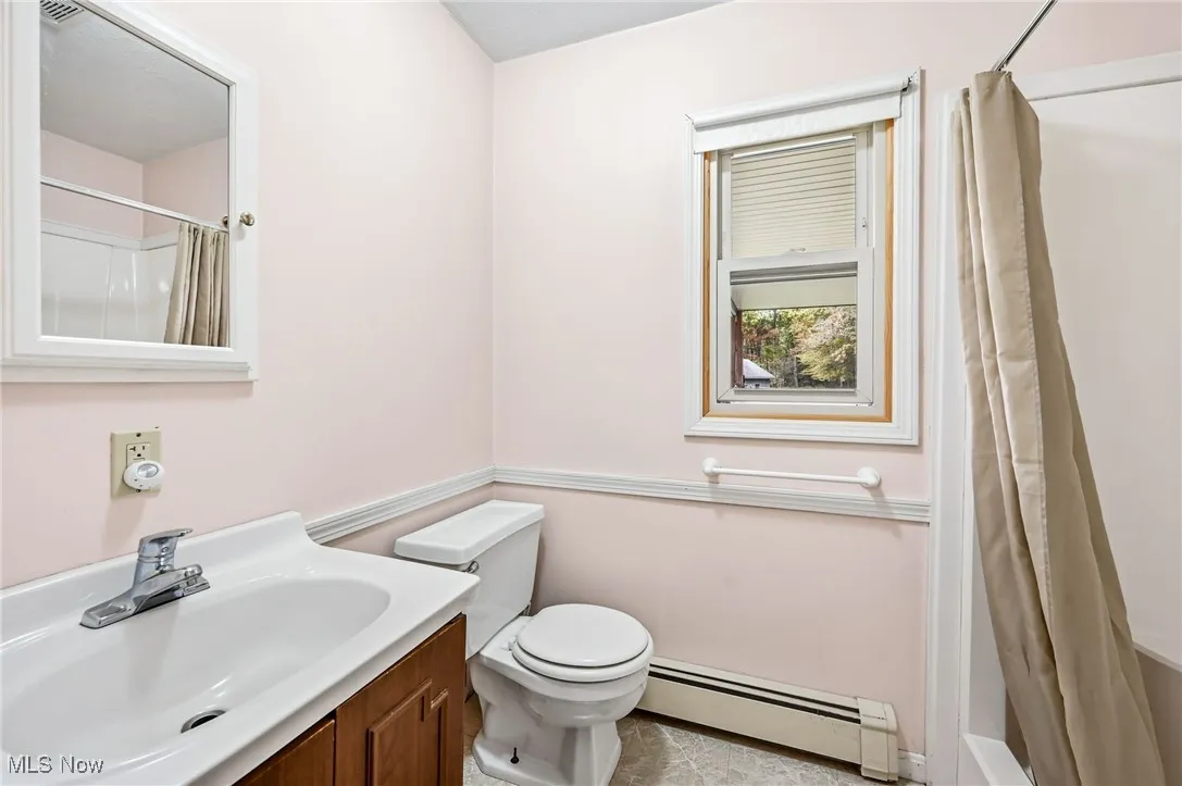 Bathroom with baseboard heating, curtained shower, vanity, and light tile patterned floors