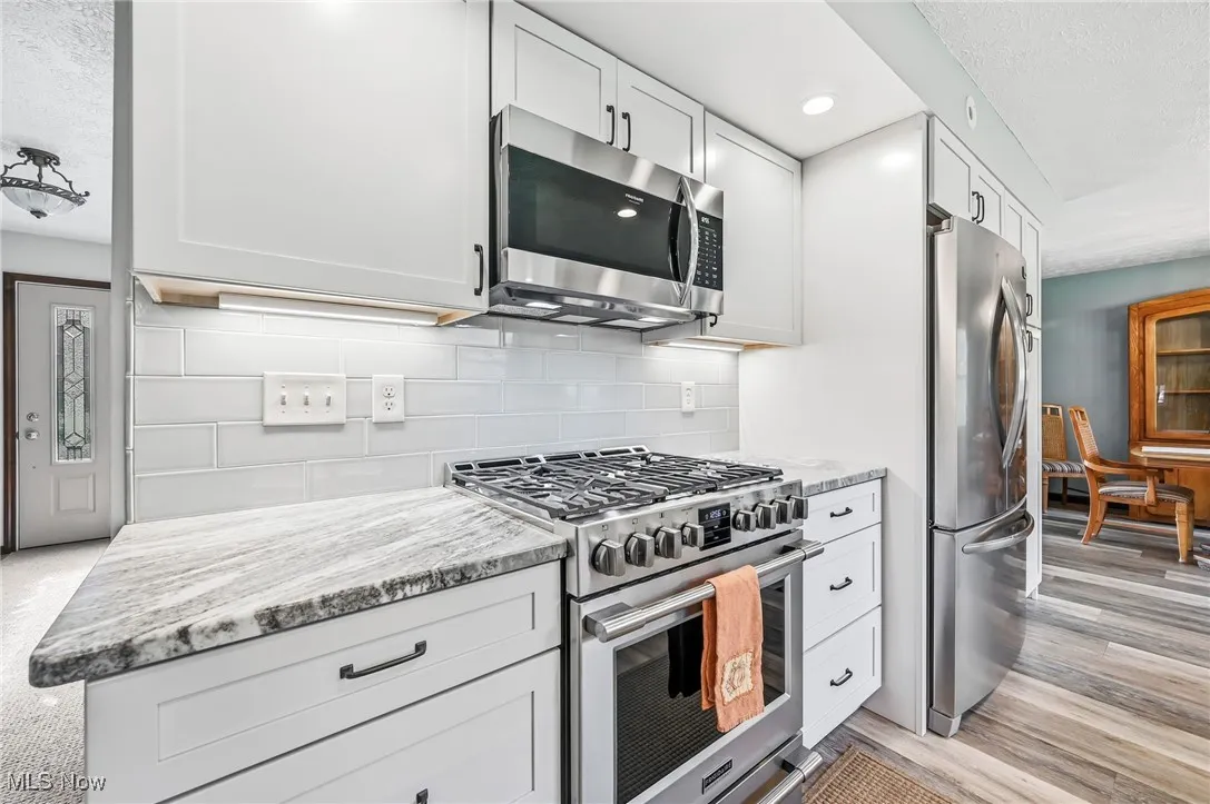 Kitchen with appliances with stainless steel finishes, a textured ceiling, light stone counters, tasteful backsplash, and white cabinetry