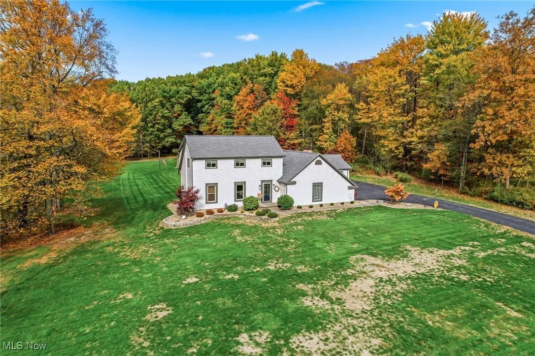 View of front of property featuring a front lawn, a forest view, and asphalt driveway