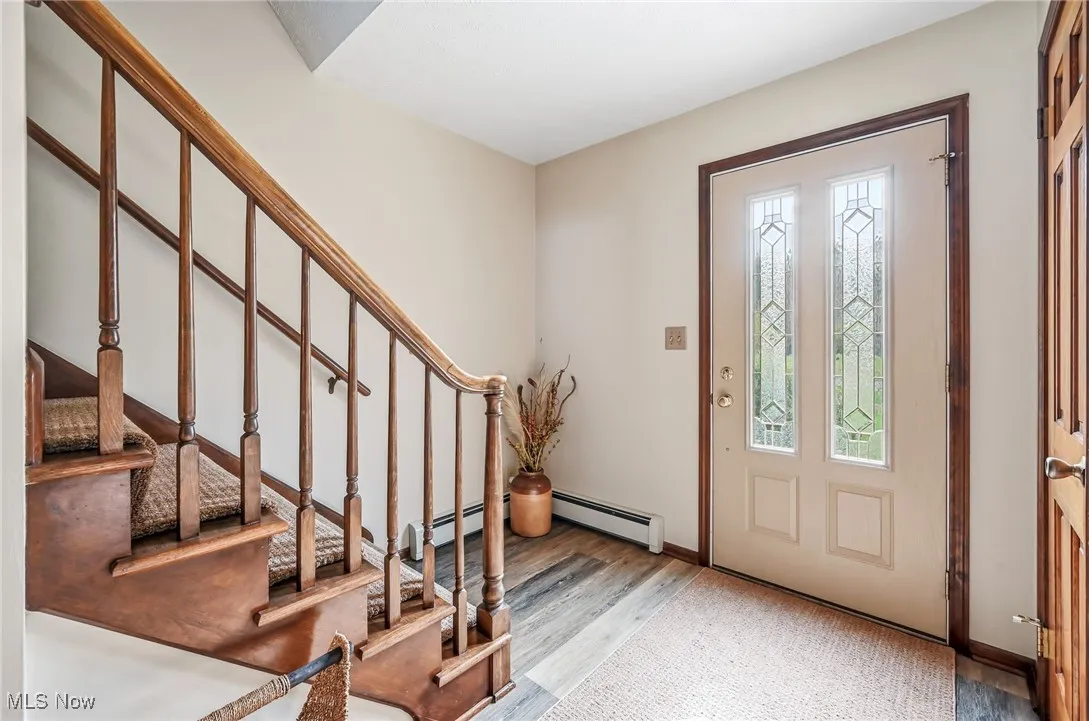 Foyer entrance featuring a baseboard heating unit, wood finished floors, and stairway
