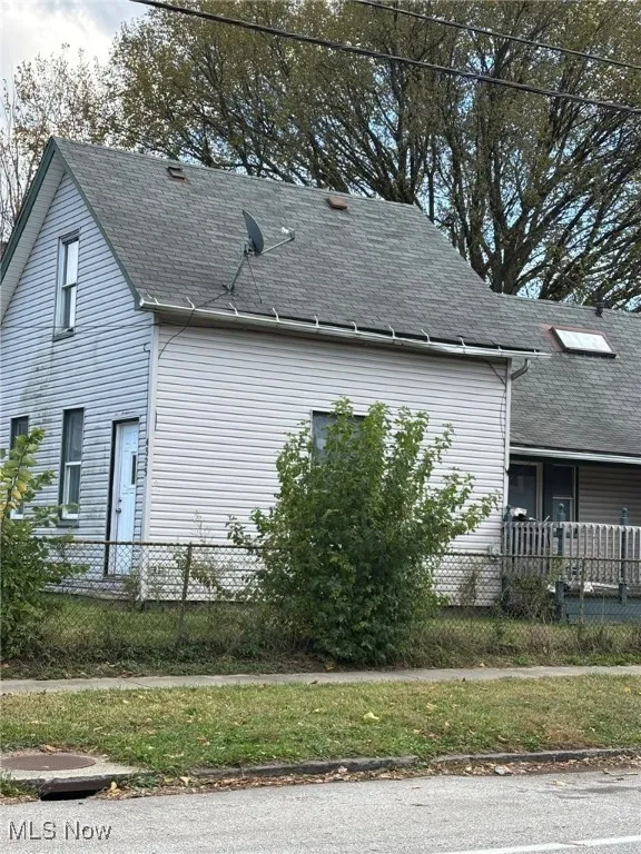 View of side of property featuring a fenced front yard and a shingled roof