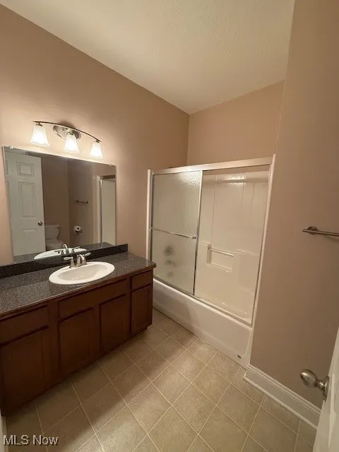 Full bathroom with combined bath / shower with glass door, vanity, and light tile patterned flooring