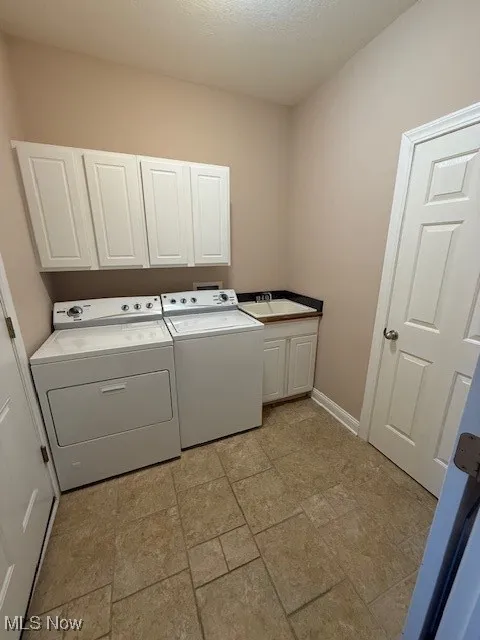 Washroom with washer and clothes dryer, cabinet space, light stone finish floors, and a textured ceiling
