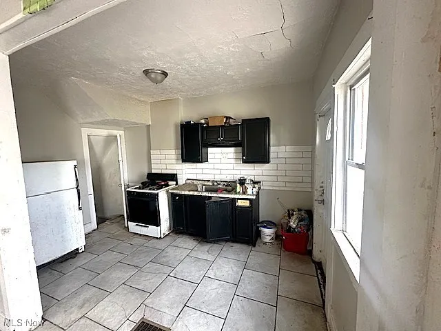 Kitchen with dark cabinets, a textured ceiling, white appliances, tasteful backsplash, and light countertops