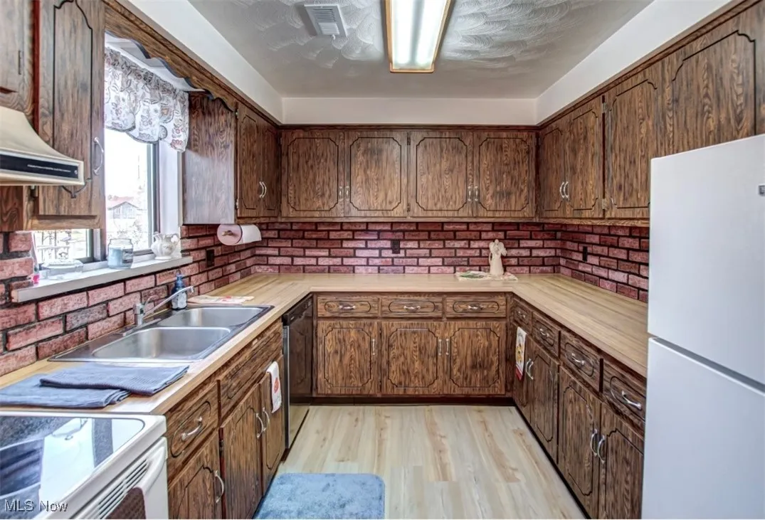 Kitchen with white appliances, light wood-style floors, light countertops, tasteful backsplash, and under cabinet range hood